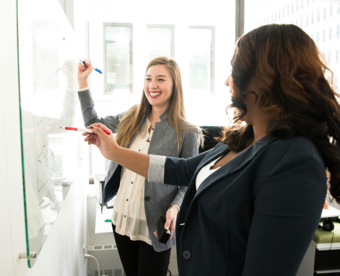 Two women are standing in front of a whiteboard.